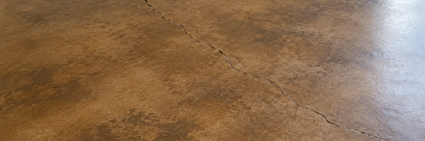 A hairline crack running across a stained concrete floor near a white baseboard